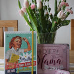 En skrivbok, en skylt och en miintask framför en bukett blommor